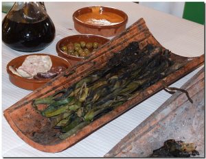 calçots en una teja con cuencos de olivas, butifarra y salsa romesco