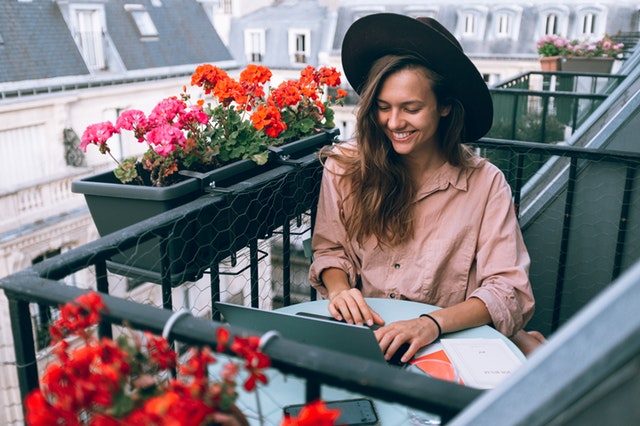 chica con sombrero sonriendo en un balcon lleno de macetas con flores