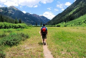 walking with a backpack on a dirt path in a field between mountains