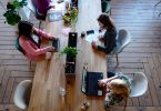 Tres mujeres sentadas e una mesa de madera delante de sus ordenadores