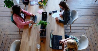 Tres mujeres sentadas e una mesa de madera delante de sus ordenadores