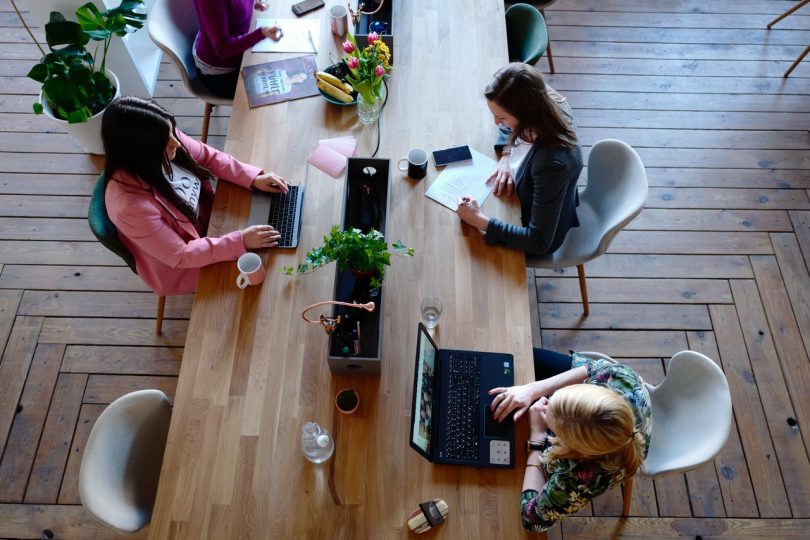 Tres mujeres sentadas e una mesa de madera delante de sus ordenadores