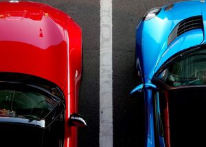 Dos coches uno rojo y otro azul separados por una línea de parquing