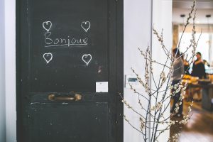 puerta en un piso con el cartel de "Bonjour" con una flor al lado