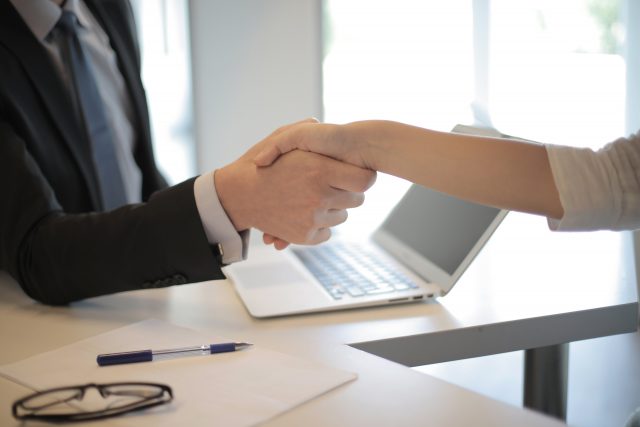 Dos personas encajando la mano con un ordenador de fondo