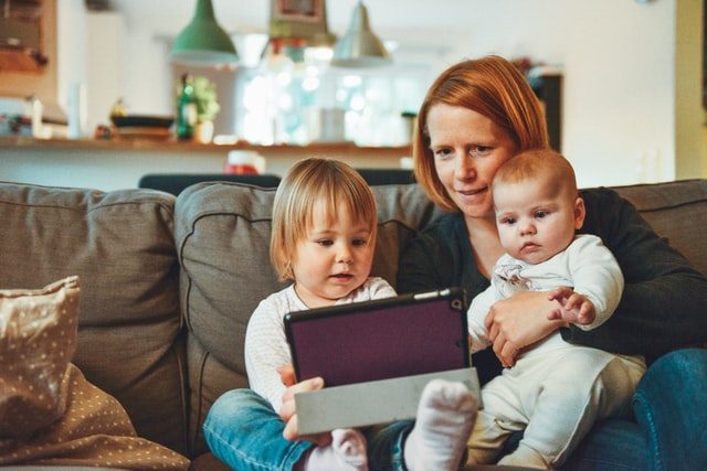 mujer sentada en un sofá con sus dos hijos mirando una tablet
