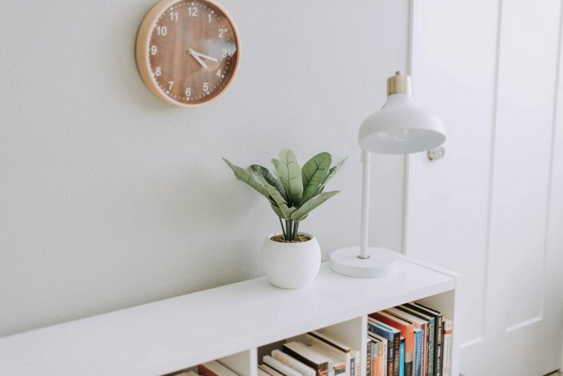 planta y lampara sobre una estanteria junto a un reloj de pared