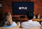 pareja en el sofá de su casa con Netflix en la televisión preprarados para hacer una maratón de series