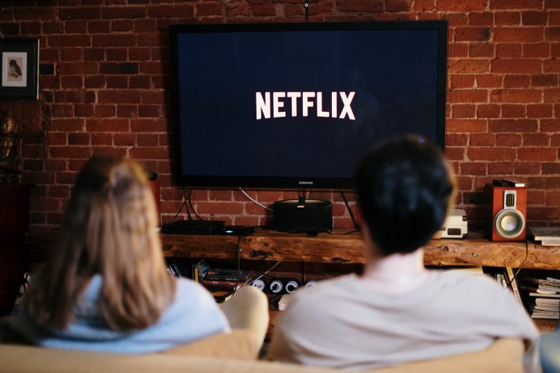 pareja en el sofá de su casa con Netflix en la televisión preprarados para hacer una maratón de series