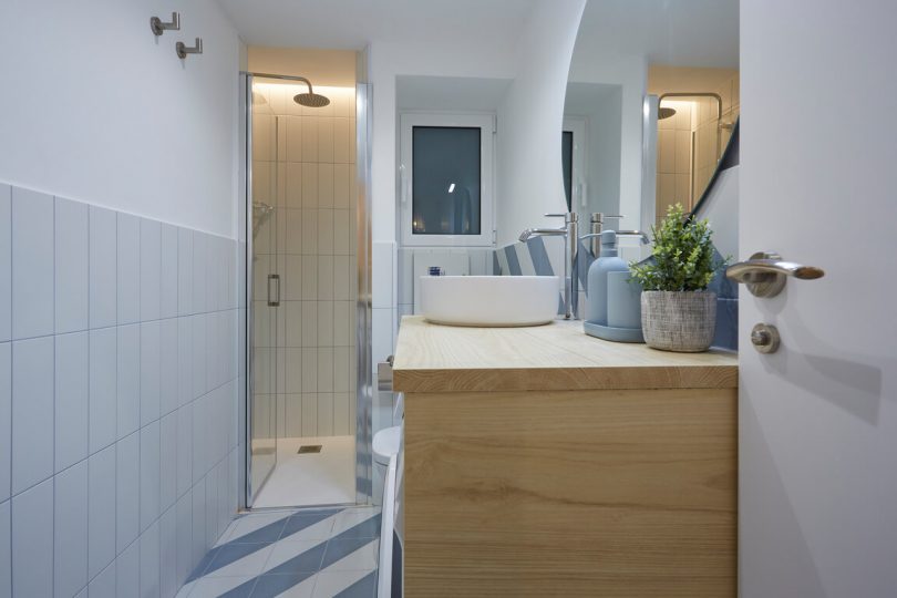Baño reformado con colores claros y muebles color madera. Plano hacia la ducha, que se integra en una estancia independiente.