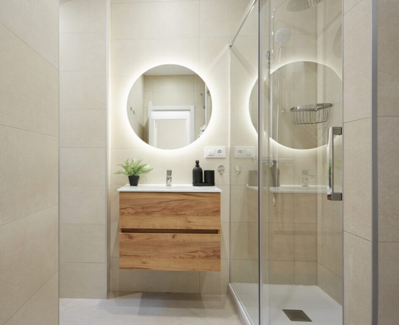 Baño reformado con colores claros y muebles color madera. Plano de detalle a la parte del friegamanos, y el espejo, con luz led integrada en el contorno.