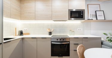 Cocina reformada con muebles blancos y color madera. Plano de detalle a la parte central, donde destaca horno y microondas, ambos integrados.