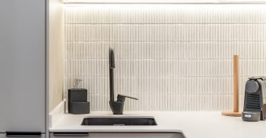 Cocina reformada con muebles blancos y color madera. Plano de detalle al grifo, de color negro.
