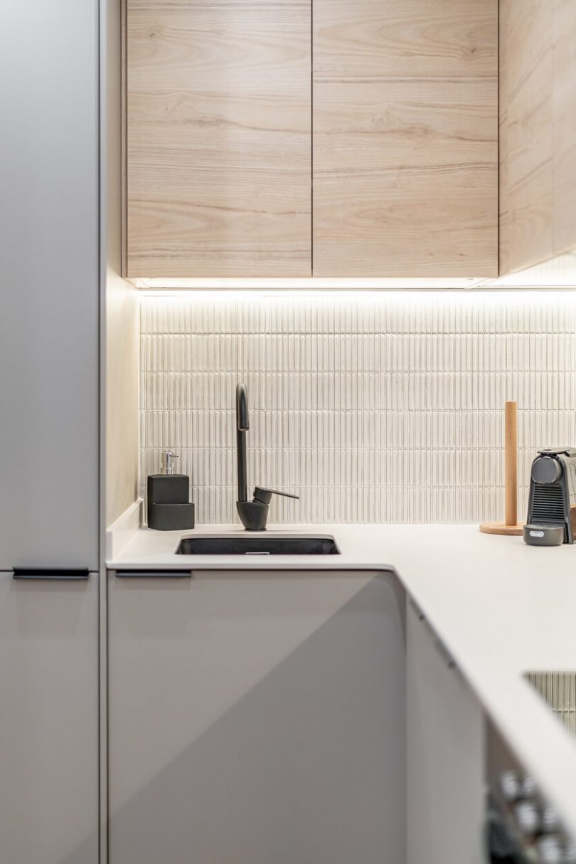 Cocina reformada con muebles blancos y color madera. Plano de detalle al grifo, de color negro.