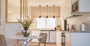 Cocina totalmente reformada, con colores blanco y crema predominantes. Una mesa con flores en primer término del plano.