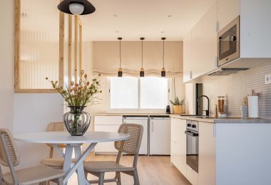 Cocina totalmente reformada, con colores blanco y crema predominantes. Una mesa con flores en primer término del plano.