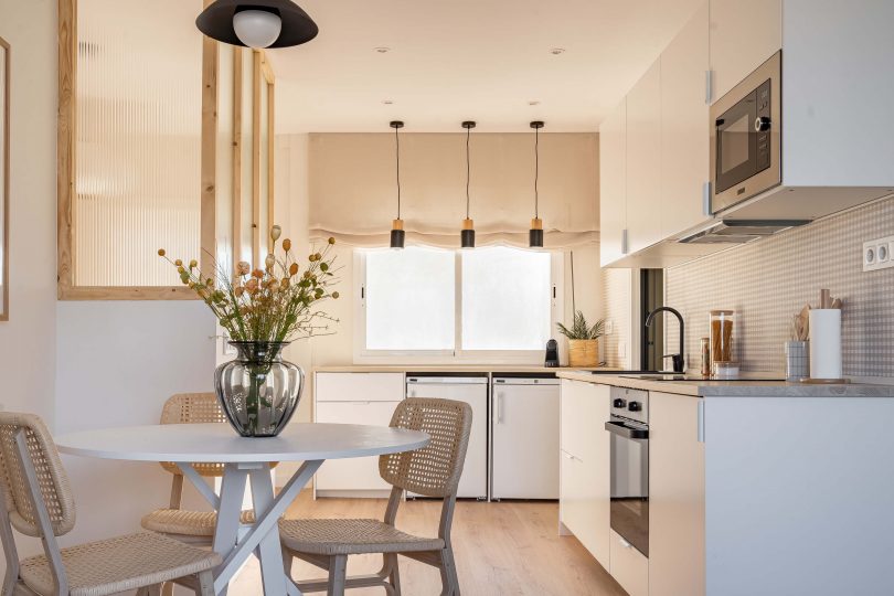 Cocina totalmente reformada, con colores blanco y crema predominantes. Una mesa con flores en primer término del plano.