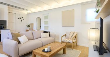 Salón reformado y completamente amueblado con suelo de parquet y colores claros.
